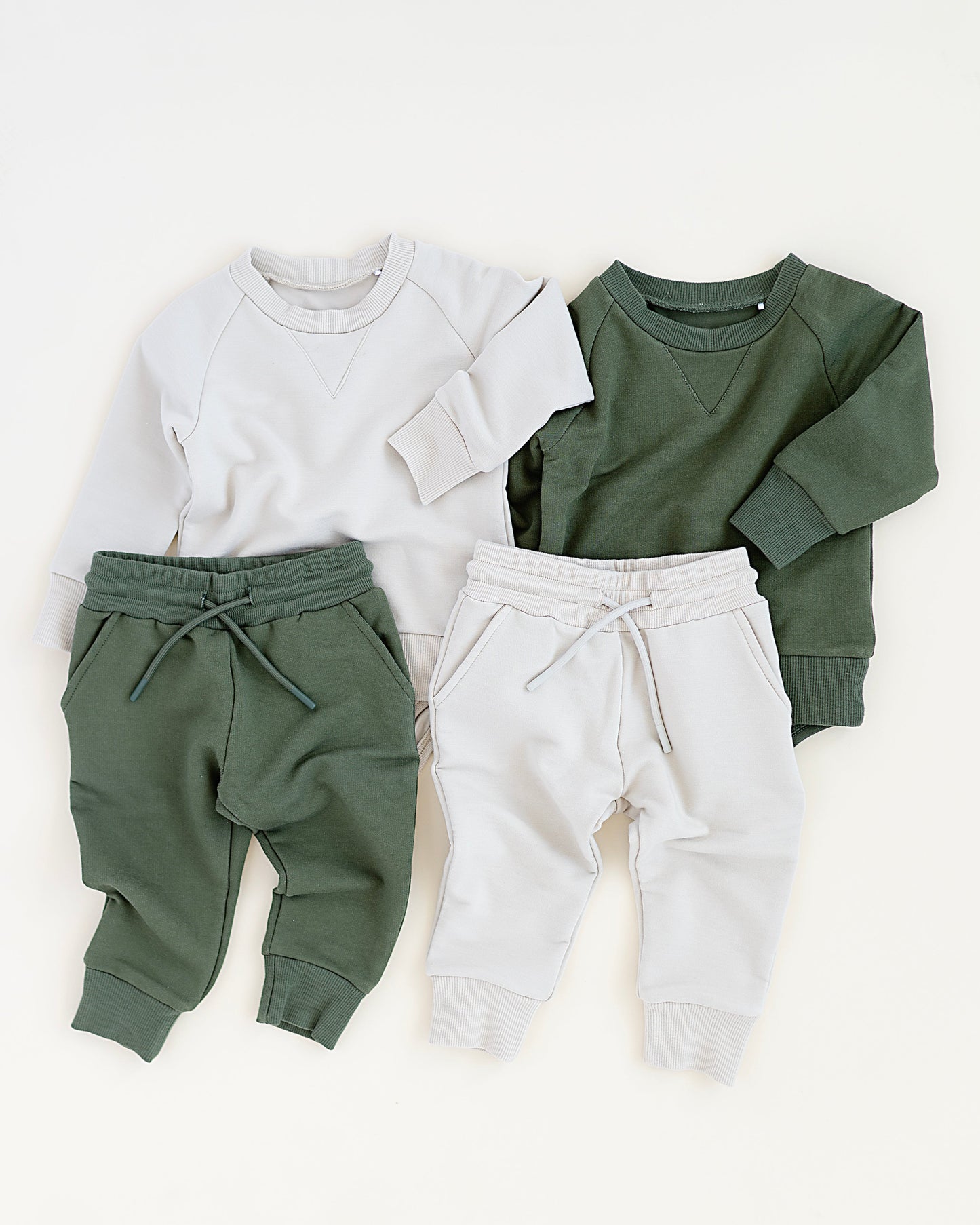 Two sets of children's clothing: a white sweatshirt with green pants and a green sweatshirt with white pants, on a white background.