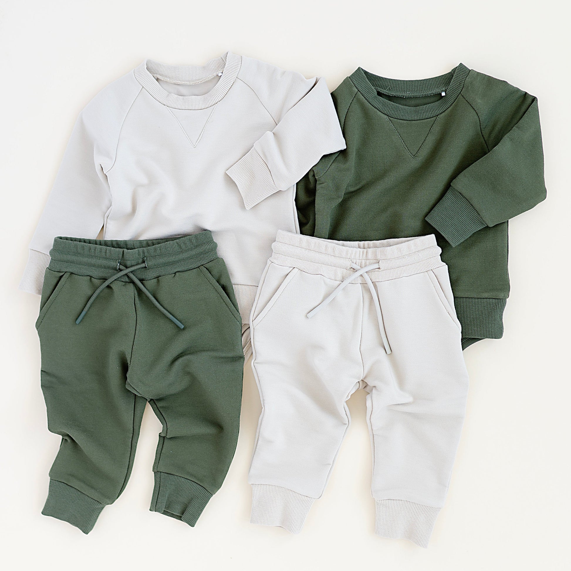 Two sets of children's clothing: a white sweatshirt with green pants and a green sweatshirt with white pants, on a white background.