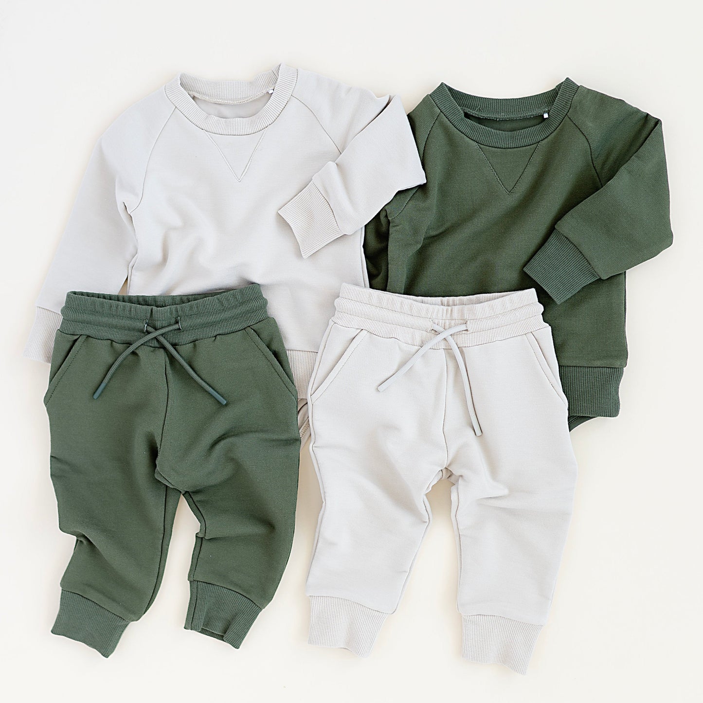 Two sets of children's clothing: a white sweatshirt with green pants and a green sweatshirt with white pants, on a white background.