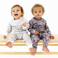 Two toddlers sitting on a wooden bench wearing matching patterned long-sleeve pajamas, photographed against a clean white studio background.