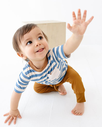 Child wearing a blue and white striped shirt and brown pants, standing on a white surface.