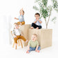 Four children sitting on and around a set of wooden blocks with a plant in the background.