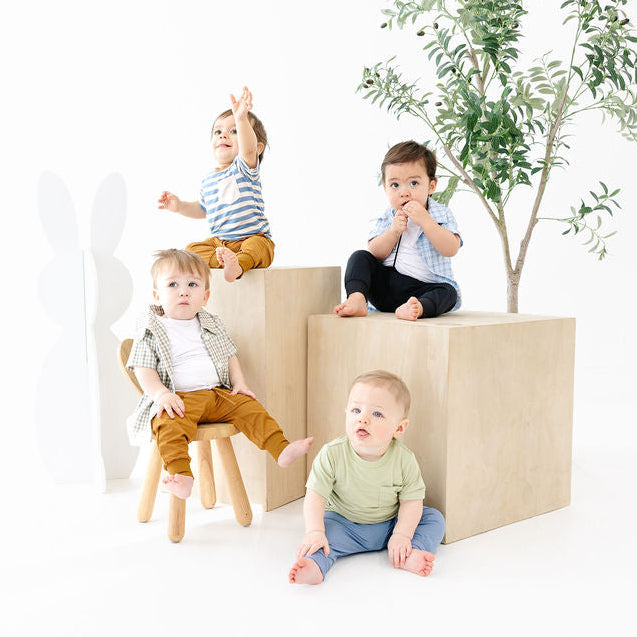 Four children sitting on and around a set of wooden blocks with a plant in the background.