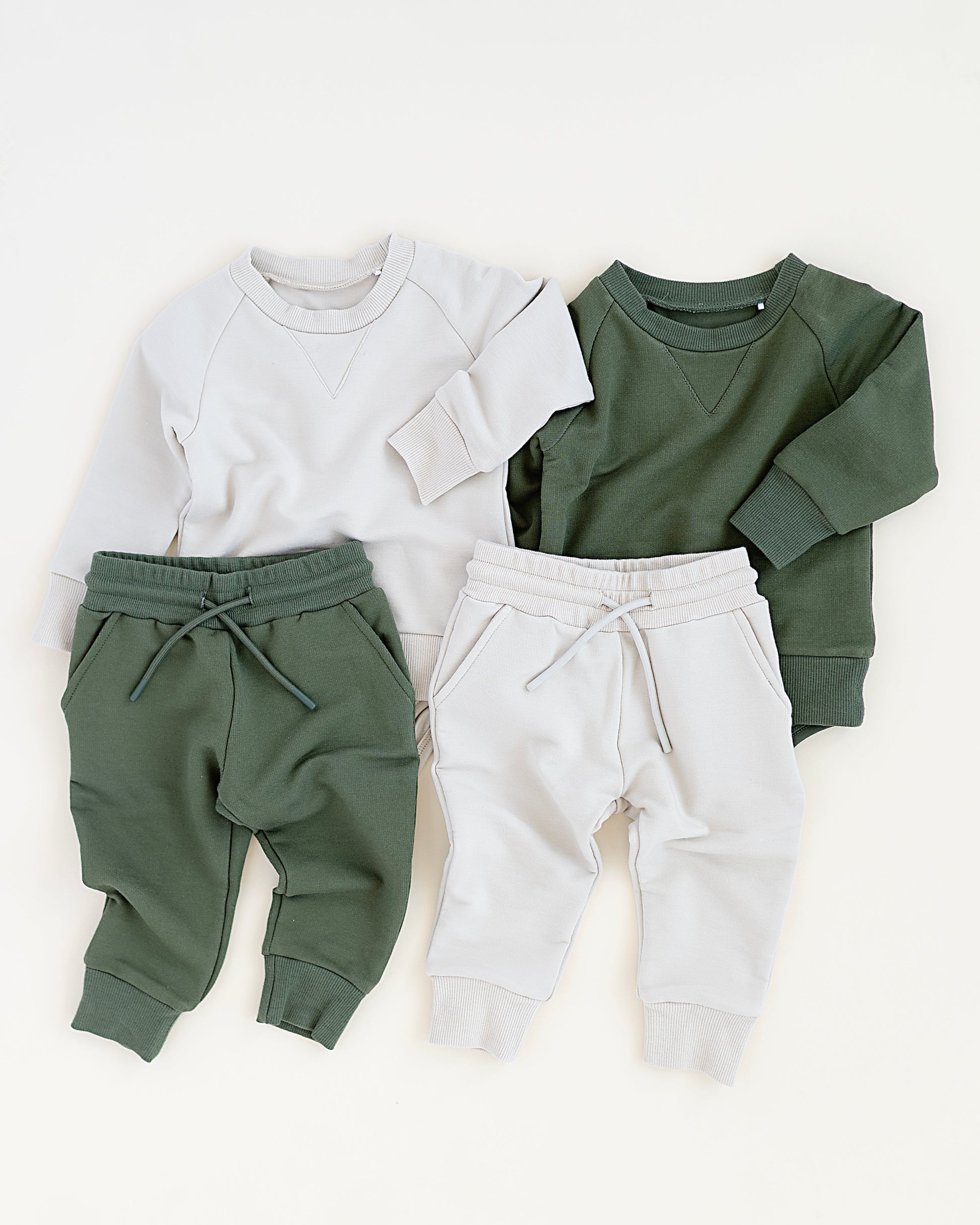 Two sets of children's clothing: a white sweatshirt with green pants and a green sweatshirt with white pants, on a white background.