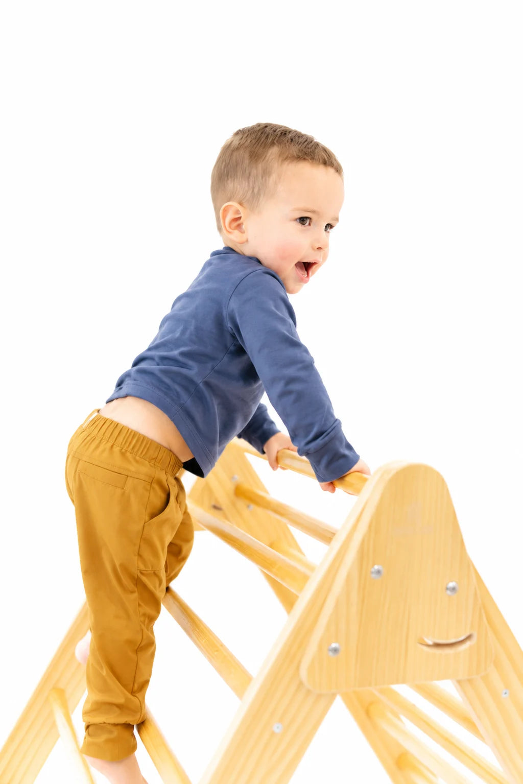 Baby in a blue shirt riding up while climbing a wooden play frame